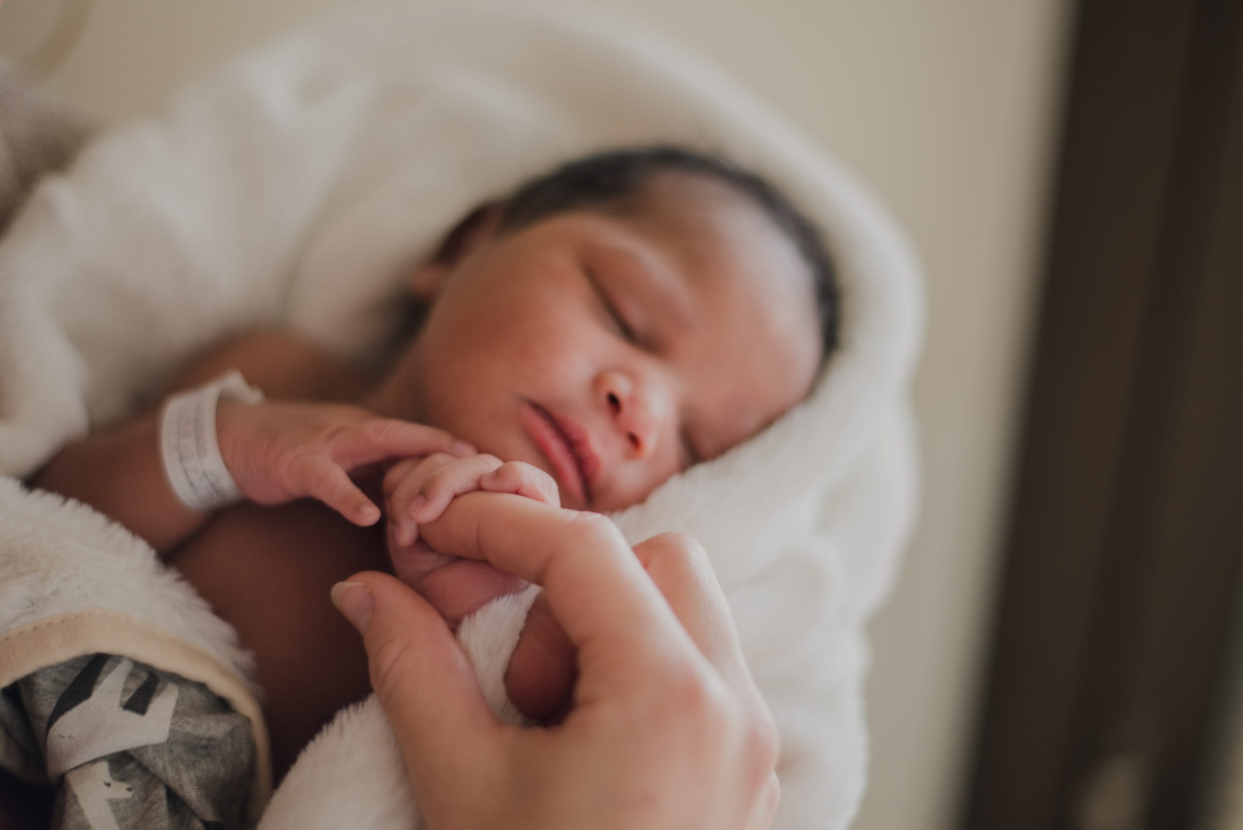 newborn baby wrapping her finger around her moms finger