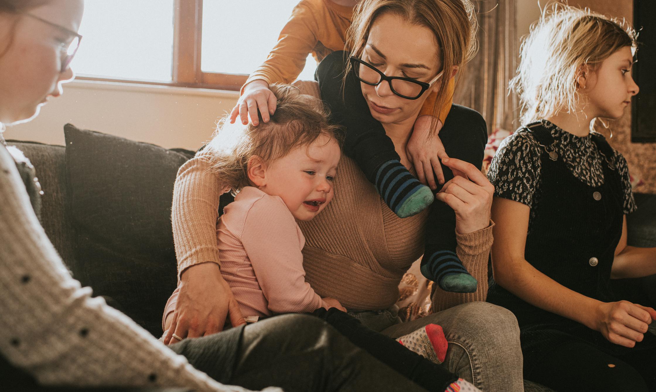 mom holding a newborn baby, a toddler on her shoulders and a child sitting next to her