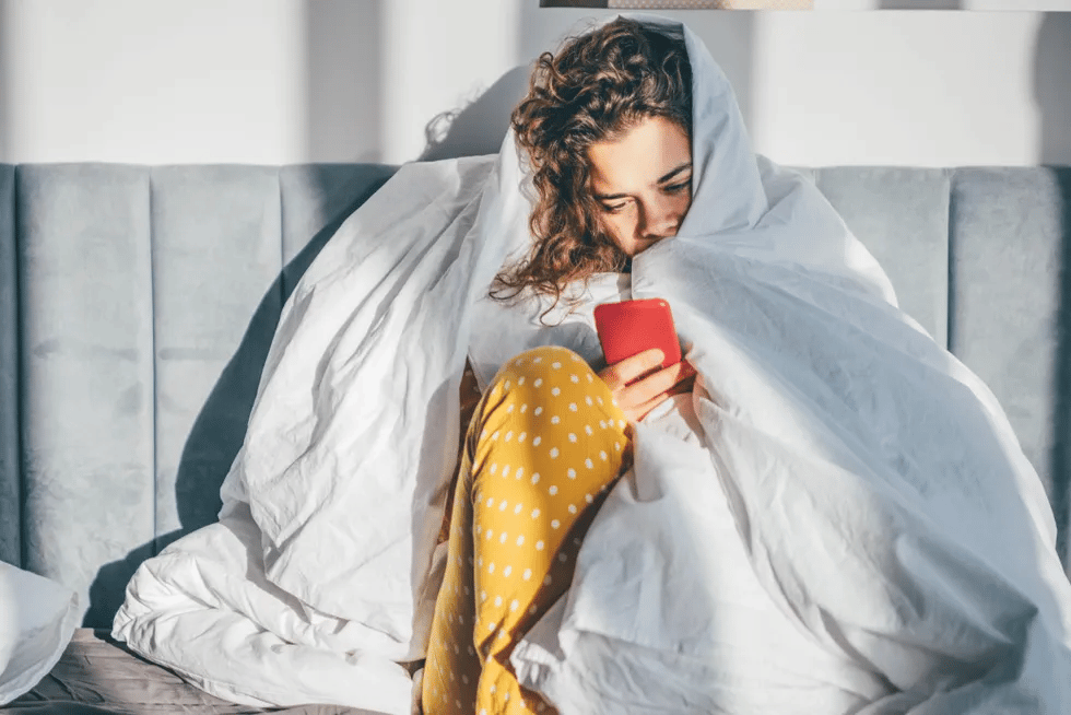 woman-under-bed-covers-looking-at-phone