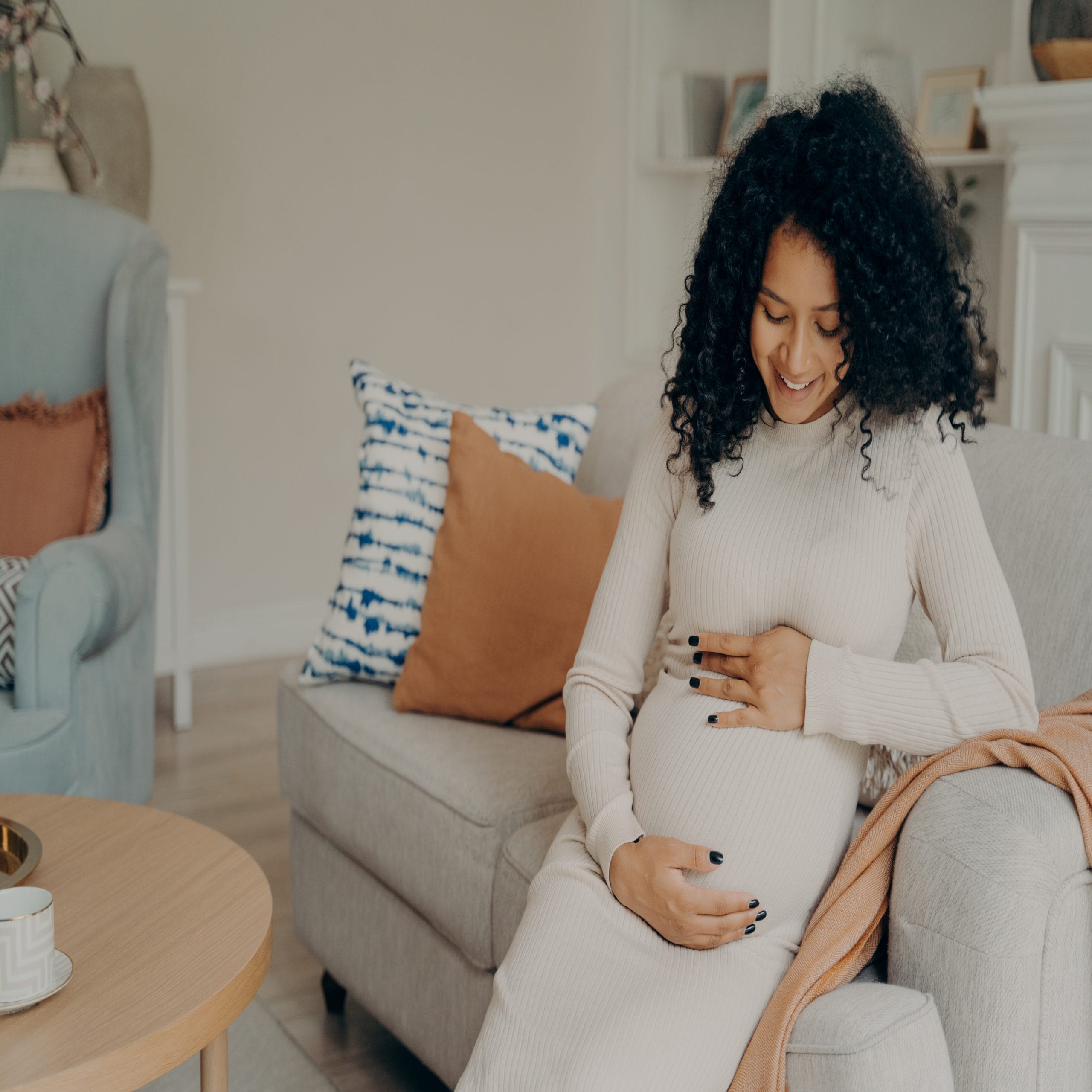 young pregnant woman holding belly on sofa