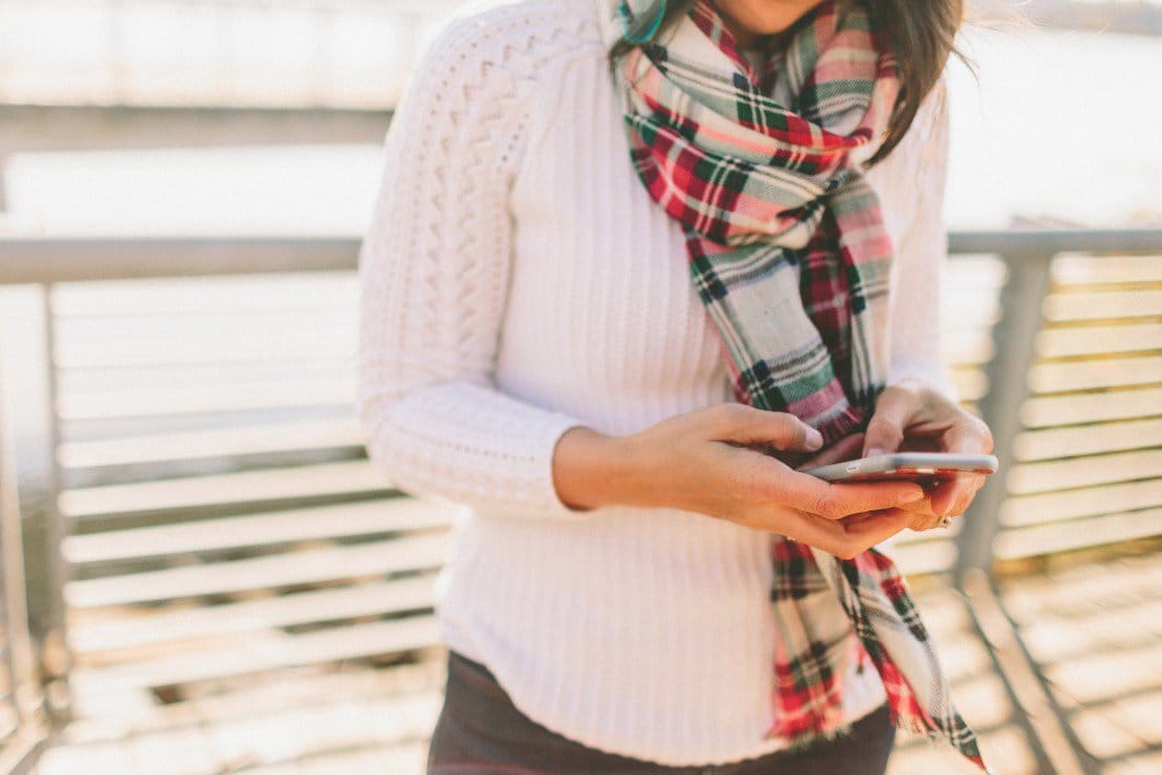 woman in plaid scarf looking at her phone for best digital gifts