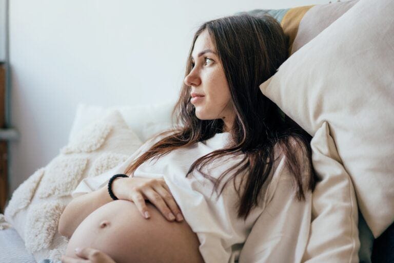 pregnant woman lying on bed with hand on belly