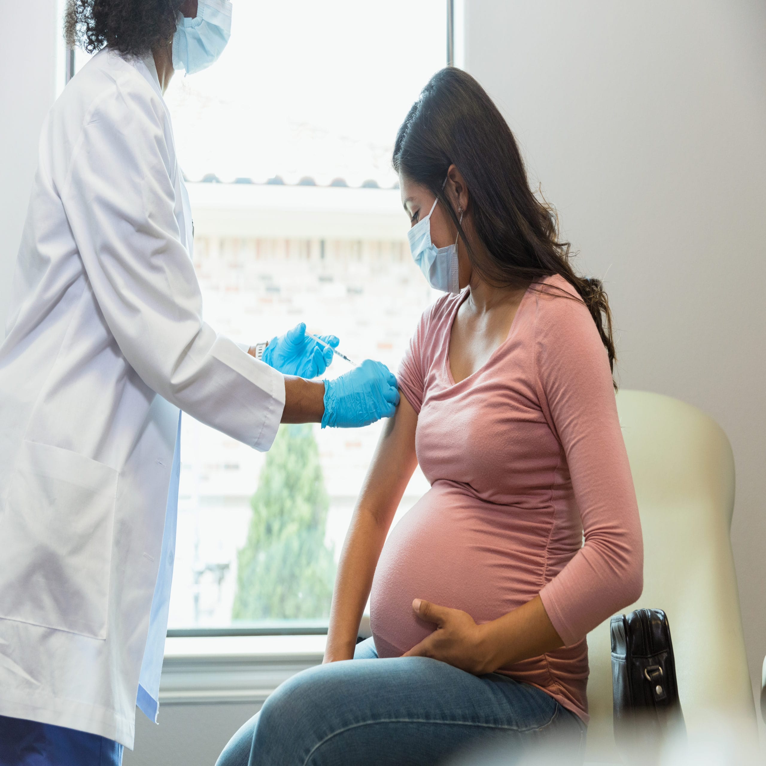 covid vaccine in pregnancy: pregnant woman watches as a doctor administers a covid booster shot