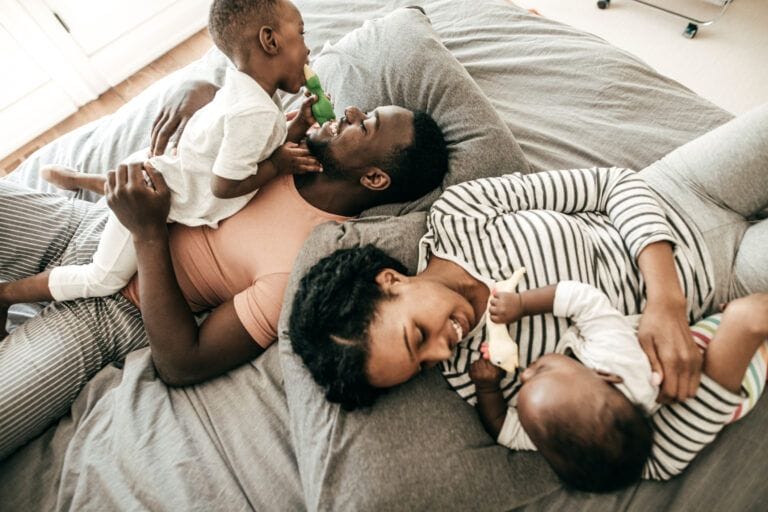 wife and husband lying on bed with two kids