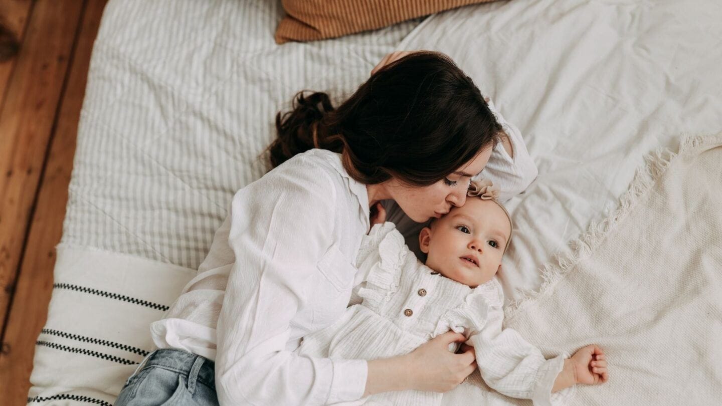 new mama: mother laying on bed kissing baby