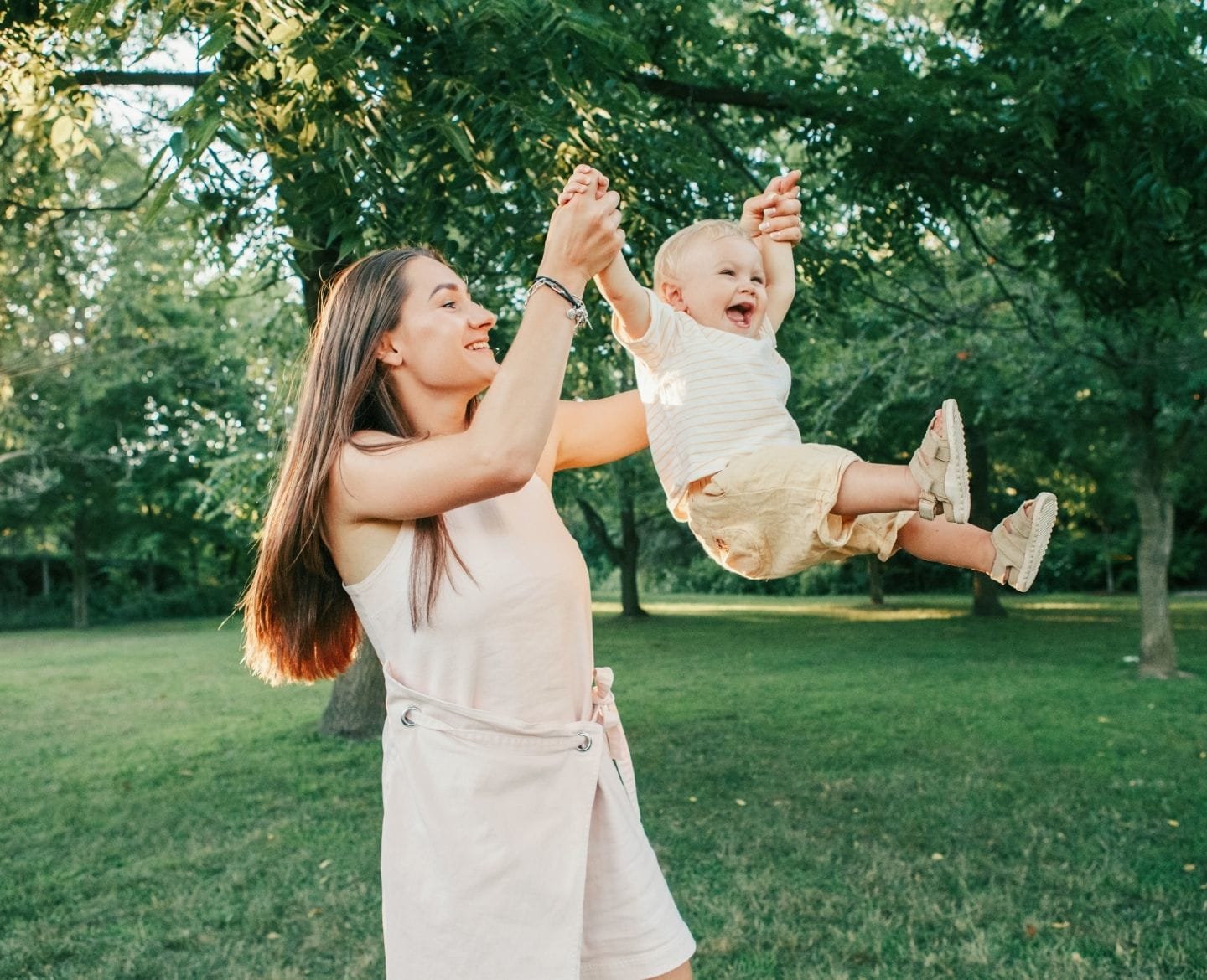 mother swinging child by the arms, celebrating her first birthday as a mom