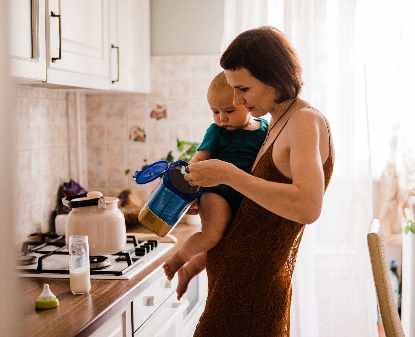 mom holding baby and scooping formula into a bottle