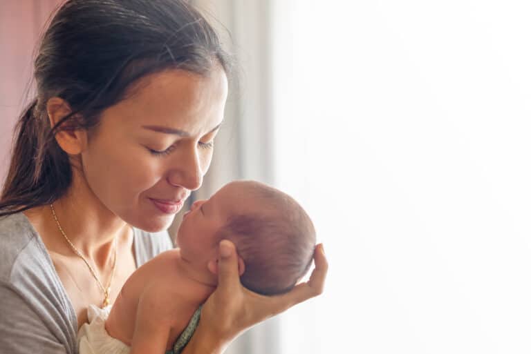 mother kissing her baby on her palm. Mother take care her little girl at home. One week newborn girl.