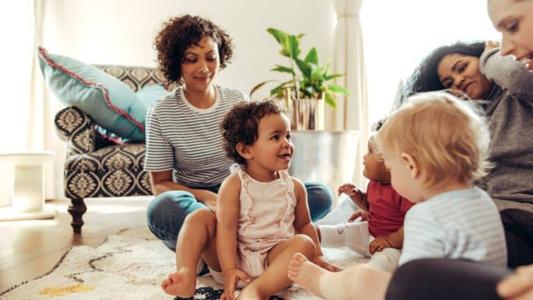 Mom friends playing with toddlers at home showing beauty of postpartum care after fourth trimester