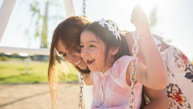 Latina mom smiling and pushing daughter on swing - Latinx mental health