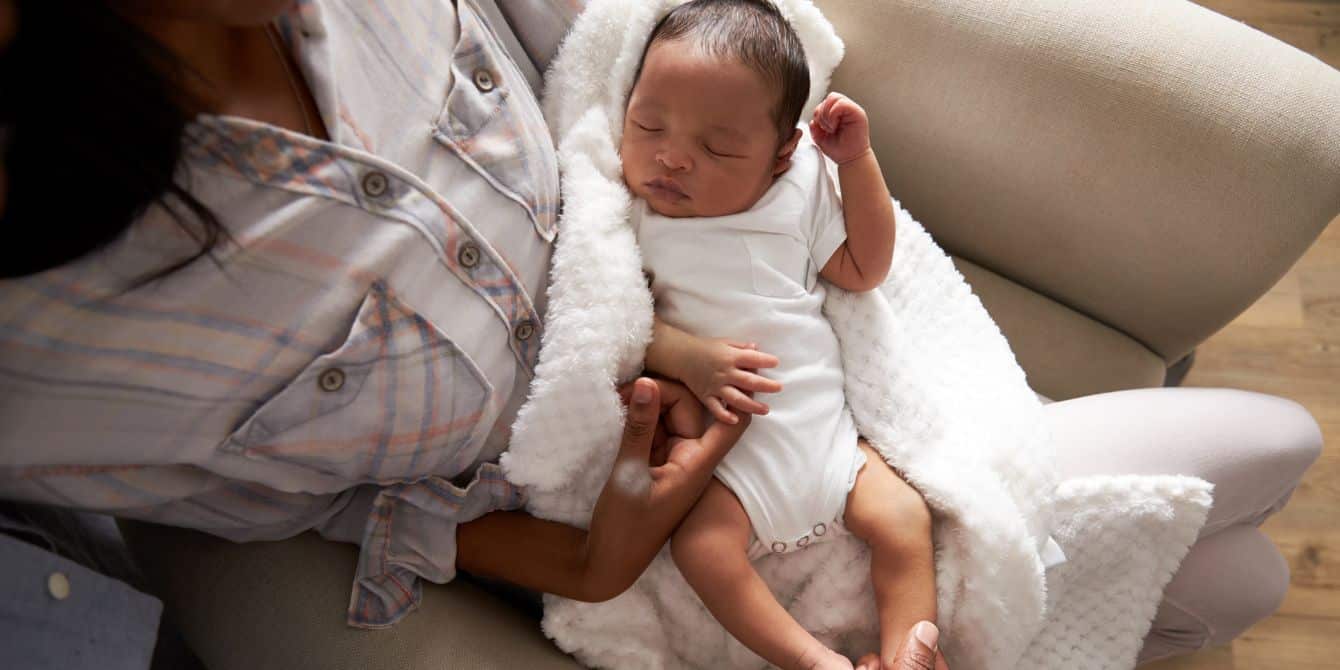 baby sleeping in mothers arms at home - walking then sitting is one way how to get a baby to sleep