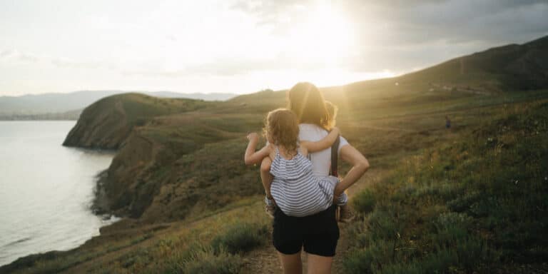 mom carrying her daughter on her back in an open field - experiences instead of gifts