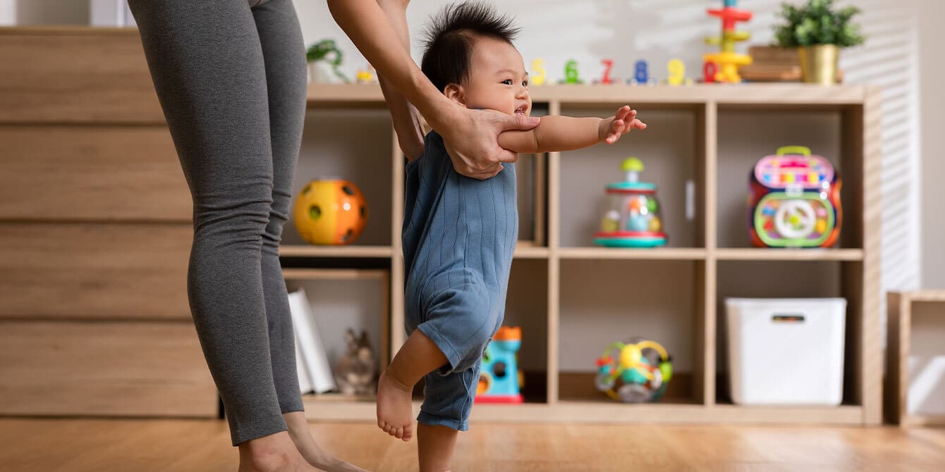 mom helping baby take first steps, wondering when do babies start walking