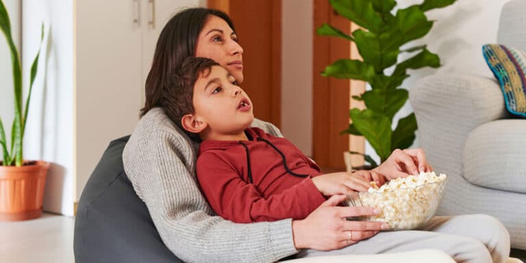 mom and son eating popcorn together watching TV - tip for after-school restraint collapse