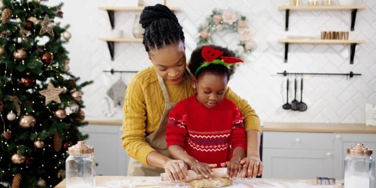 mom helping daughter roll cookie dough - family christmas traditions