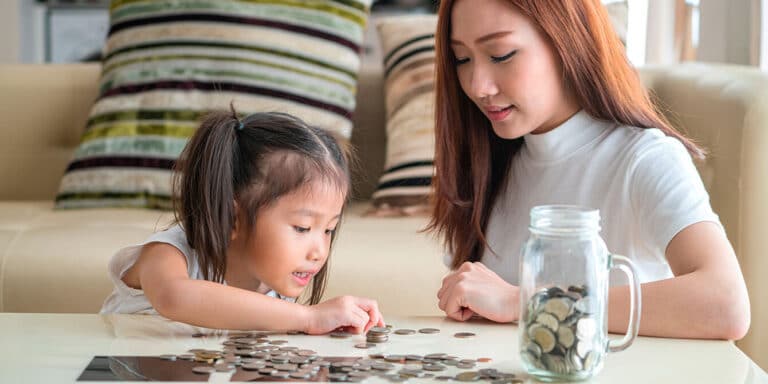 Mom and daughter counting coins from a jar learning about money.