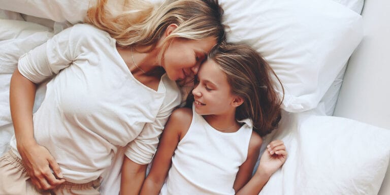 mom and daughter laying in bed laughing co-sleeping with older kids