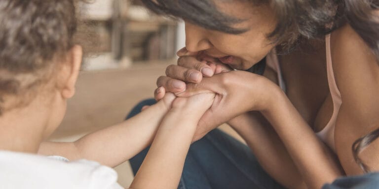 mom kissing her baby's hands - reducing medical trauma in kids around fear of needles