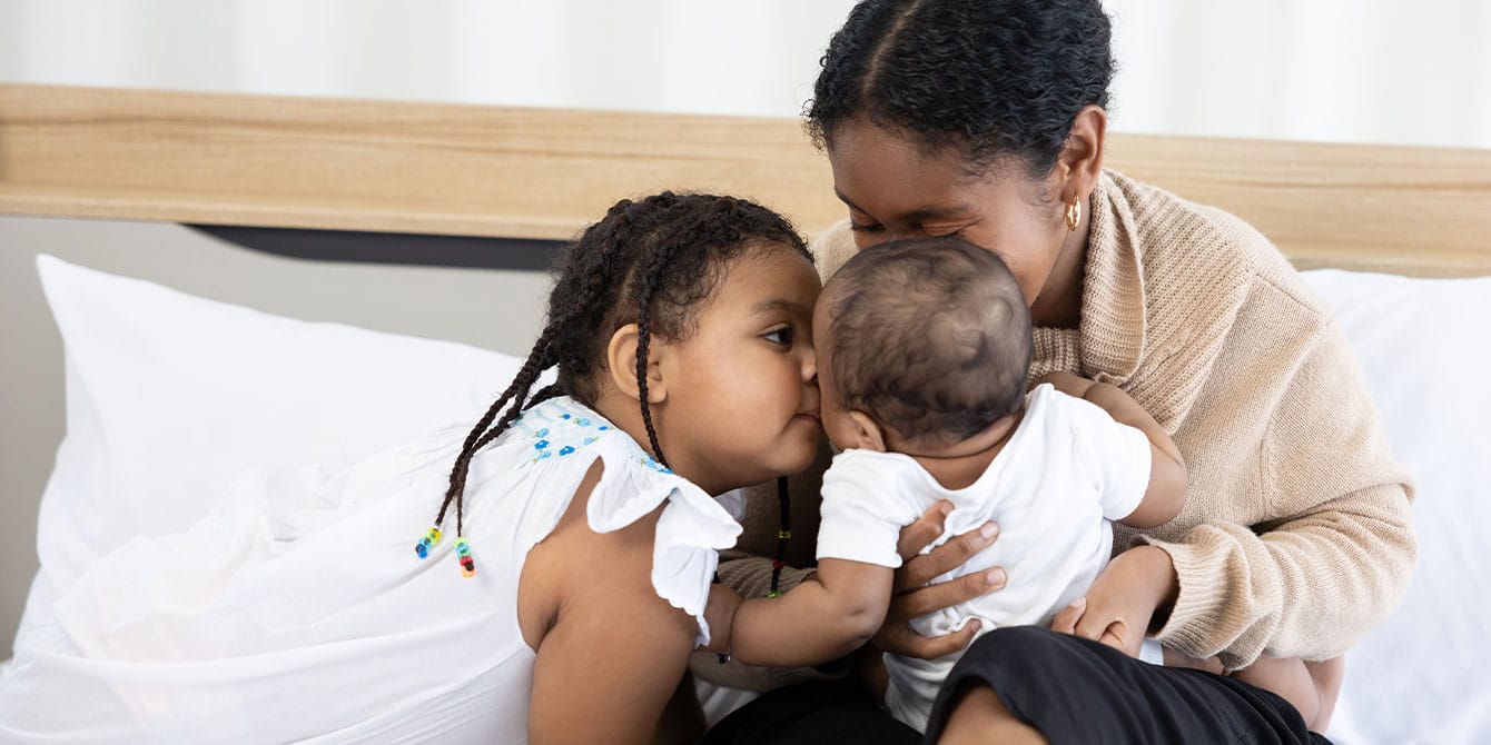 mom parenting and cuddling child and baby on a bed