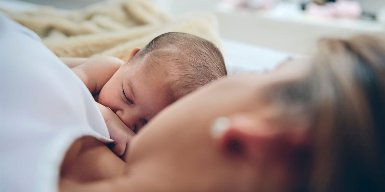 newborn baby held by mother while bedsharing - cosleeping and bedsharing