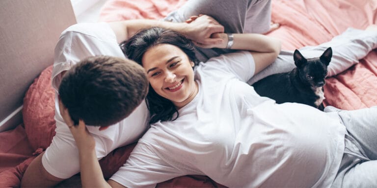 pregnant couple laying in bed with dog - postpartum hotel or babymoon