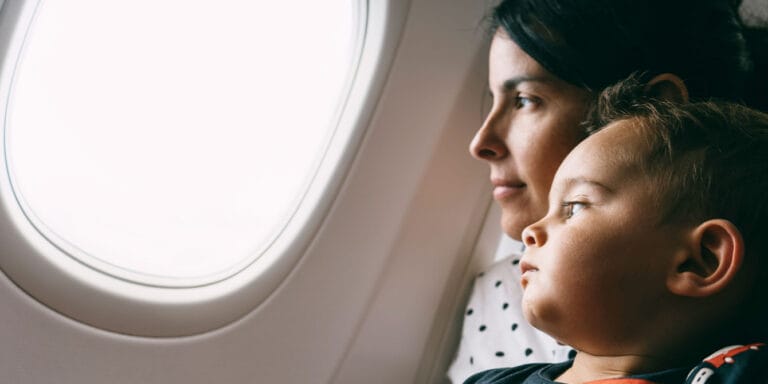 young mother flying with a toddler holding son and looking through aircraft window