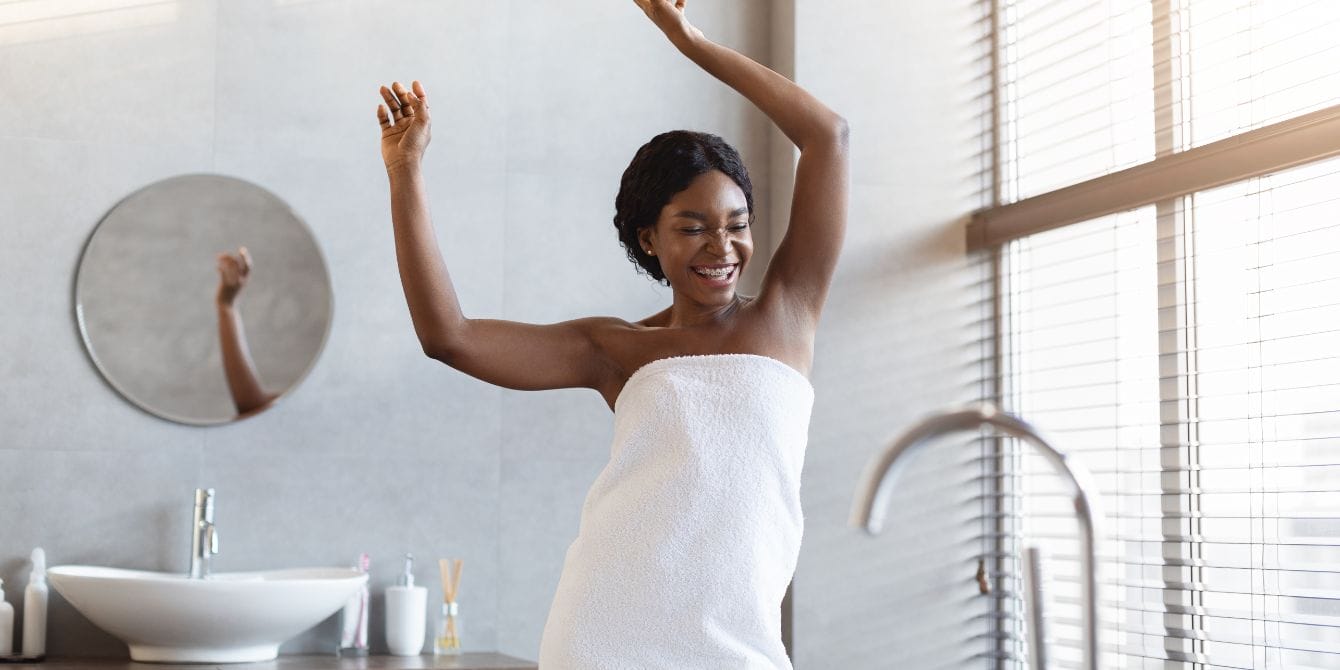 happy woman covered in white towel dancing and laughing in modern bathroom