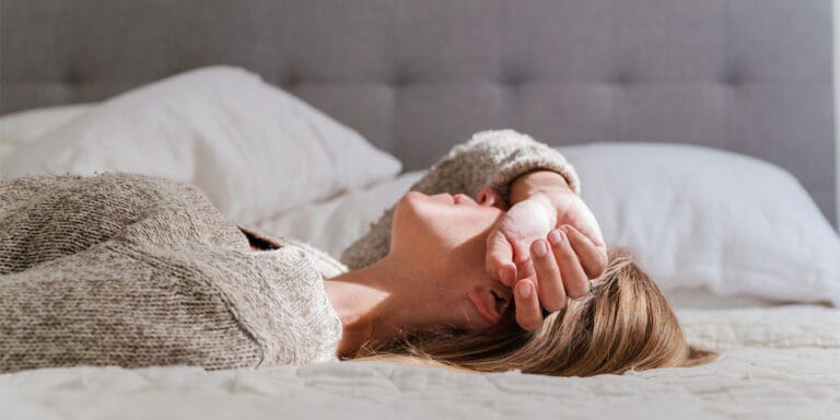 woman laying on her bed covering her eyes-missed miscarriage