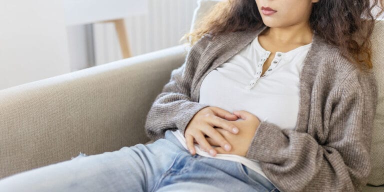 woman in discomfort holding her stomach on the couch - cryptic pregnancy