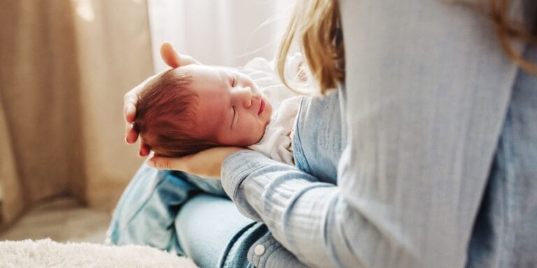 mother holds newborn baby in lap at home - top newborn questions