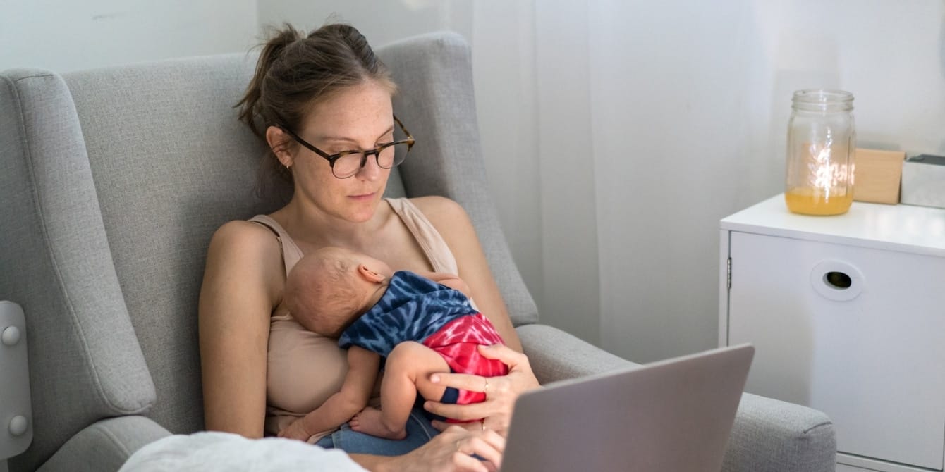 mom holding infant on chest while using laptop - online mom groups