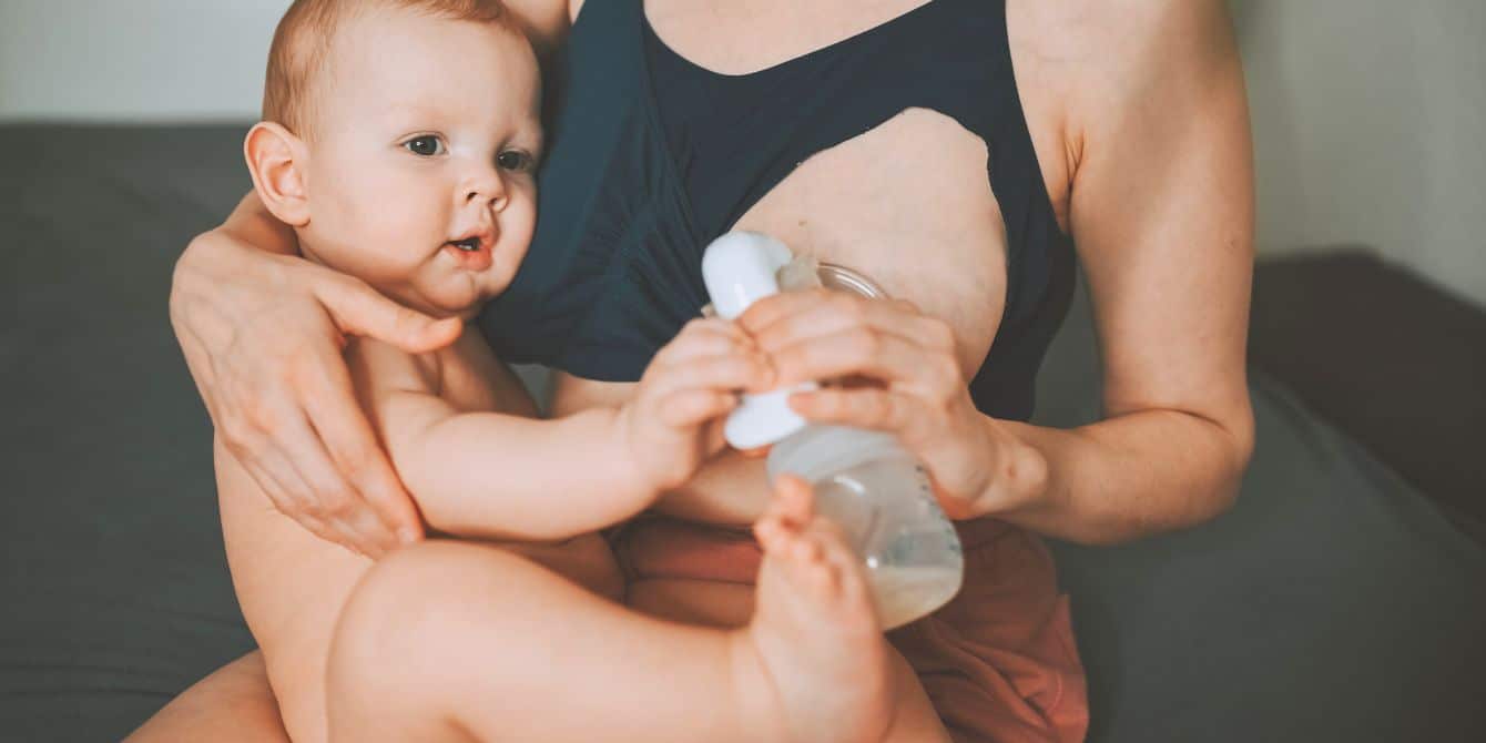 mom using manual breast pump while holding baby