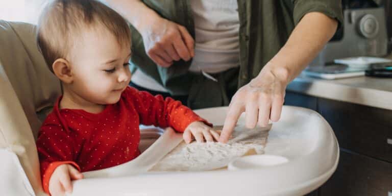 baby sitting in high chair doing sensory play with flour - benefits of sensory play