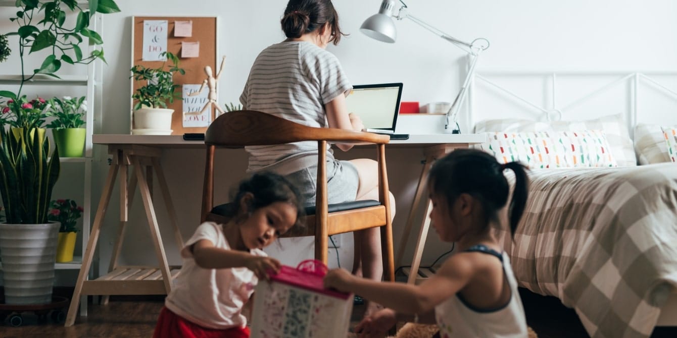 mom working from home on a laptop while kids play around her- wfh mom