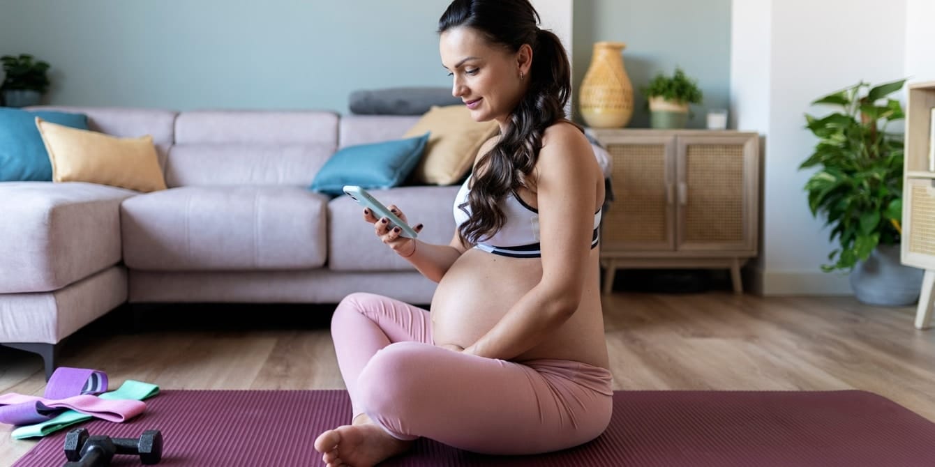 pregnant woman with phone on yoga mat - pregnancy workout apps