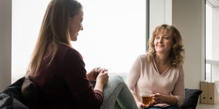 Mother talking to her teen daughter while having tea at home - parenting young adults