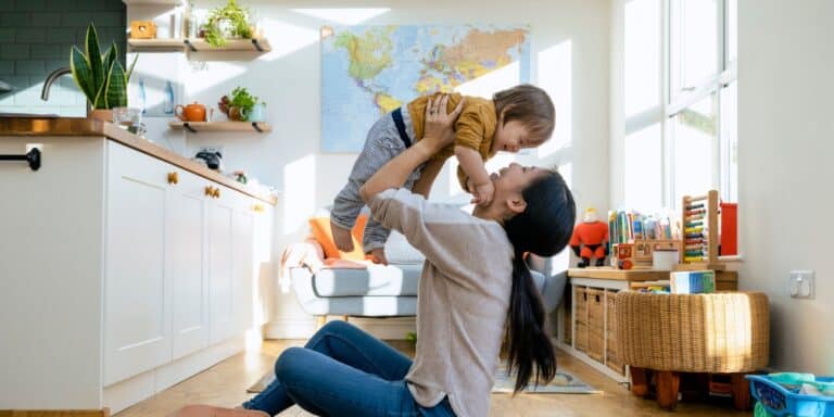 mother sitting on floor holding toddler boy in air - learning a second language