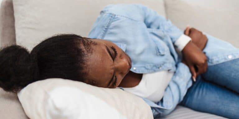 woman laying on sofa sick holding pelvis - period products