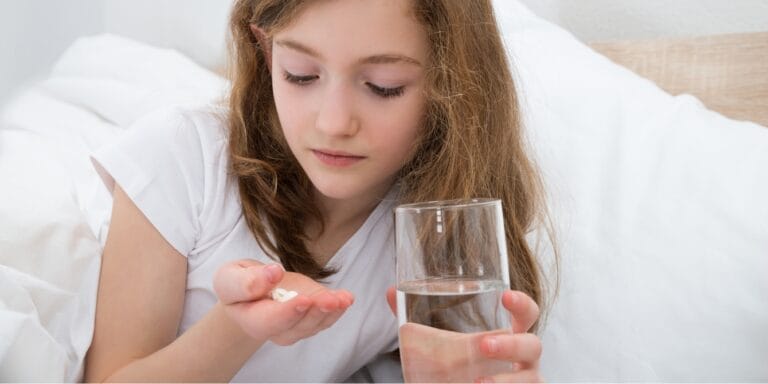 girl in bed taking pills with glass of water melatonin use is rising in kids