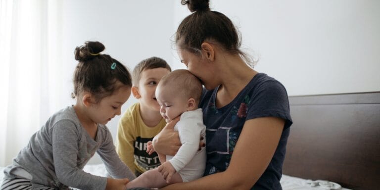 mom holding baby with two older kids new sibling relationships