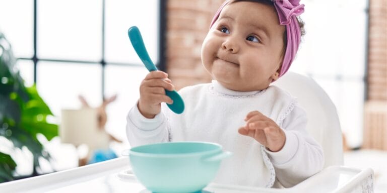 baby sitting in high chair holding spoon 90-90-90 rule