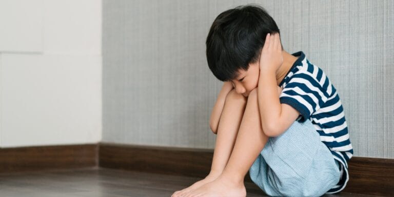 little boy sitting in corner covering his ears sensory processing disorder