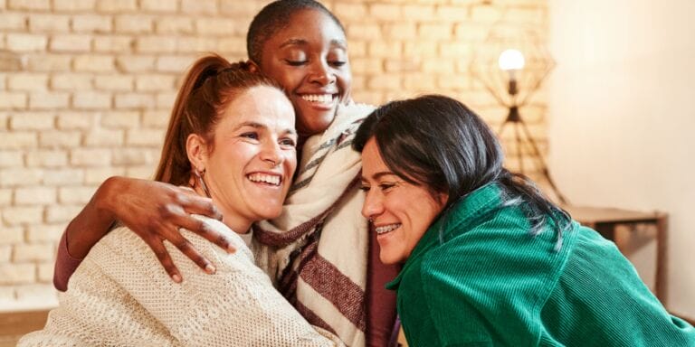 female friends hugging in living room making mom friends