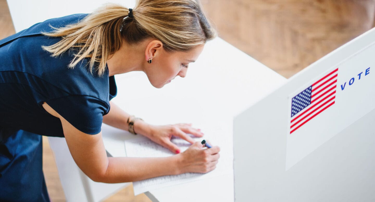 woman filling out election ballot - register a mom to vote day