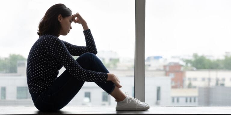 woman sitting in a corner with knees up and hands on her head