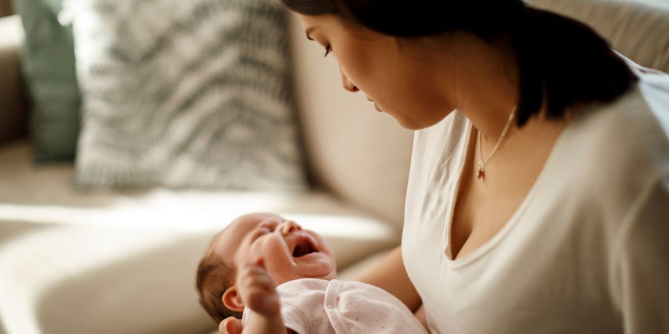 mom holding newborn alone at home - pathologizing motherhood - Motherly