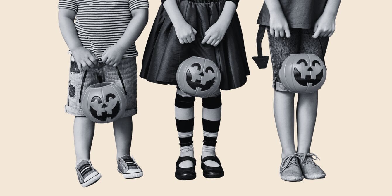 Three little kids standing in a row carrying Halloween candybuckets