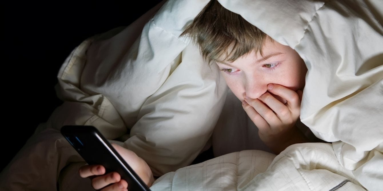 Child on the phone under the covers at night in bed